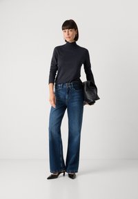 Mørk grå høyhalset genser, høyt liv, brede blå jeans og svarte spisse hæler. Holder en svart veske. Jevne teksturer, avslappet passform.
