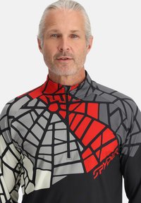 Langarm, met rits, top in zwart, grijs en rood met geometrische patronen en het "Spyder" logo aan de rechterbenedenkant. Gladde textuur.
