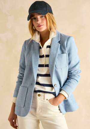 Light blue herringbone blazer with a collar and two front pockets. Paired with a white and navy striped polo and light-colored pants.