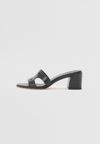 Sandali a soffietto neri in pelle con tacco a blocco, caratterizzati da una punta aperta e tagli laterali, con una texture liscia e un design minimale.