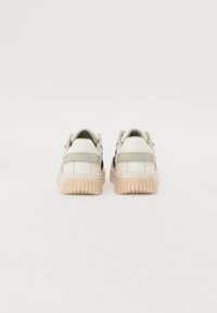 Hvide sneakers med en tekstureret overflade, kontrasterende sorte detaljer og en gummisål med vandrette riller. Set fra bagfra.
