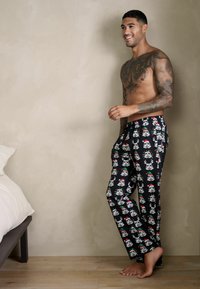 Fekete pizsamanadrág, amelyet egy ismétlődő mintázat díszít, rajzfilmszerű rohamosztagosok téli kiegészítőkkel, puha anyagból készült.