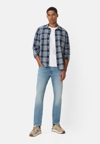 Geruite langlopende shirt in marineblauw en wit, gedragen over een wit t-shirt, in combinatie met lichtblauwe jeans en beige sneakers.