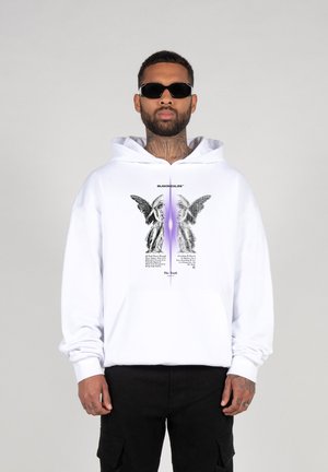 White hoodie with a central graphic of angel figures and text. Features a front pocket and ribbed cuffs. Model wears black sunglasses.