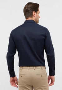 Marineblauwe overhemd met lange mouwen en een button-down kraag, gladde textuur, en met knoopsluitingen bij de manchetten, gecombineerd met lichtbeige nette broek.