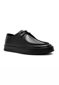 Zapato de cuero negro con punta redonda, superficie lisa y diseño minimalista. Presenta un sistema de cierre con cordones y una suela gruesa.