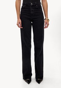 Vaqueros de mezclilla negros de talle alto con un ajuste recto, que cuentan con trabillas para el cinturón, cierre de botón en la parte frontal y una tela ligeramente texturizada.