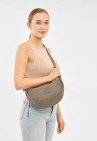 Borsetta a tracolla khaki con un design morbido e arrotondato, dotata di un patch con logo frontale e di una tracolla regolabile, realizzata in tessuto resistente.