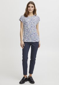 Bloemmotief top in wit, blauw en groen, met korte mouwen en een ronde halslijn. Gecombineerd met slim-fit marineblauwe broeken en zwarte schoenen.