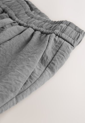 Pantaloni scurți gri cu talie elastică, confecționați dintr-un material moale, cu pliuri și o textură ușor cutată. Marginea este finisată îngrijit.