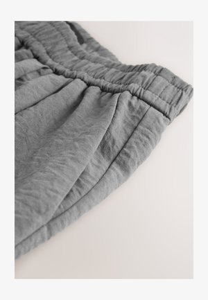 Pantaloni scurți gri cu talie elastică, confecționați dintr-un material moale, cu pliuri și o textură ușor cutată. Marginea este finisată îngrijit.