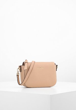 Beige strukturierte Leder-Umhängetasche mit verstellbarem Riemen und goldenem Verschluss, liegend auf einer weißen Oberfläche vor einem schlichten weißen Hintergrund.