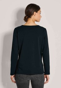 Schwarzes Langarmshirt mit Rundhalsausschnitt und glatter Textur. Entworfen für einen lockeren Sitz, in graue Jeans gesteckt.
