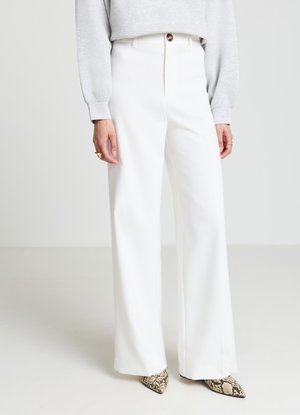 Pantaloni bianchi a gamba larga con vita alta, dotati di chiusura frontale con bottoni e tessuto dalla texture liscia. Abbinati a una maglia grigia a maniche lunghe e tacchi con motivo decorativo.