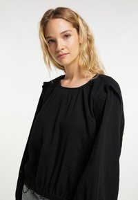 Zwarte katoenen blouse met lange mouwen, textuurstof, geplooide schouderdetails en een ronde halslijn, met een aansluitende taille.