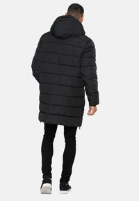 Schwarze Daunenjacke mit Kapuze, ausgestattet mit einem gesteppten Design und langer Länge. Das Material wirkt glänzend und verfügt über einen Reißverschluss vorne sowie Seitentaschen.