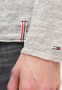 Maglione grigio a maglia con una finitura testurizzata. Presenta un piccolo dettaglio di design con strisce rosse, bianche e blu all'orlo e alle maniche.