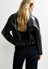 Veste bombardier en cuir noir avec une coupe décontractée, ourlet côtelé et détails aux épaules. Portée avec un jean bleu foncé.
