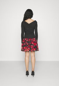 Top nero a maniche lunghe con retro a V, abbinato a una gonna svasata con un motivo floreale rosso su sfondo nero. Scarpe nere con tacco alto.