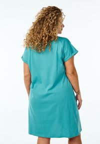 Robe turquoise à manches courtes en tissu doux, présentant une coupe décontractée et un col rond. Texture lisse avec des manches roulées.