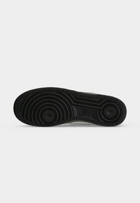 Μαύρη λαστιχένια σόλα παπουτσιού Nike με κυκλικά σχέδια πέλματος και το λογότυπο της Nike στη μέση κάτω από το πόδι, εμφανιζόμενη σε απλό γκρι φόντο.