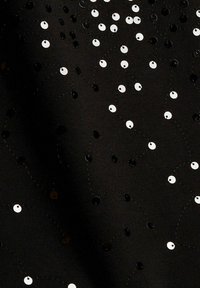 Černá látka s rozptýlenými černobílými kulatými flitry spojenými jemným černým stehem v zvlněném vzoru. Měkká textura.