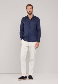 Camisa de botones azul marino en una tela suave, combinada con pantalones blancos y espadrilles negros. Corte recto con mangas largas y cuello puntiagudo.
