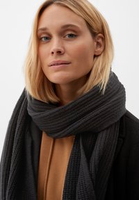 Sciarpa a maglia grigia scura con una texture a coste, avvolta attorno al collo, abbinata a una maglia marrone e a un cappotto nero.