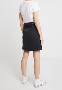 Černá džínsová sukně s rovnými liniemi, střední délky, zadní kapsy a lemem se značkou, zkombinovaná s bílým tričkem a bílými teniskami.