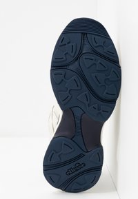 Suola delle scarpe con un design in gomma navale testurizzata, caratterizzata da motivi scanalati e un logo. Il materiale sembra resistente con una forma robusta.