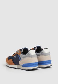 Zapatillas multicolores que combinan paneles de ante marrón, gris y azul marino, con un acento azul en la suela y detalles en el logo.