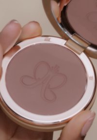 Compact poeder met een lichtbruine kleur en een reliëf ontwerp van een vlinder. Zilveren en roségouden accenten op de verpakking. Smooth textuur.