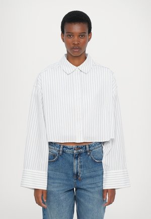 Hvid kortærmet skjorte med blå lodrette striber, knaplukning foran, brede manchetter og en klassisk krave, parret med lyseblå højtaljede jeans.