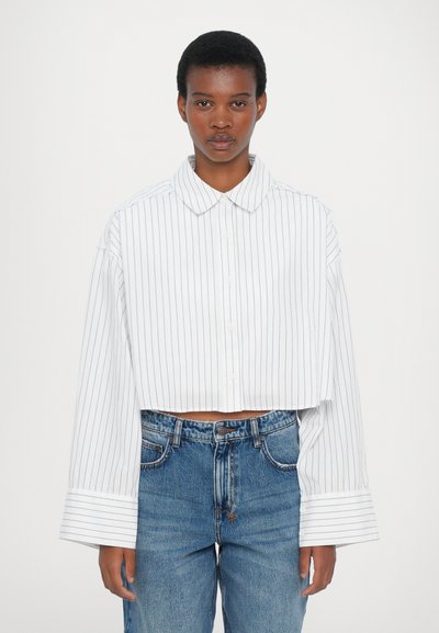 White cropped shirt with blue vertical stripes, button-down front, wide cuffs, and a classic collar, paired with light blue high-waisted jeans.