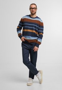 Maglione a maglia con strisce marroni, blu e arancioni; abbinato a pantaloni blu scuro e sneakers bianche. Tessuto a trama con polsini a coste.
