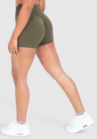Olijfgroene hoge taille shorts met een aansluitend ontwerp. Zacht, rekbaar materiaal; gladde textuur; gecombineerd met witte sneakers en zichtbare enkelsokken.