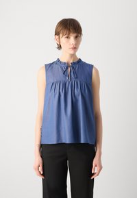 Ανοιχτό μπλε αμάνικο τοπ με βολάν στον λαιμό, λεπτομέρεια με κλειστό λαιμό και συγκεντρωμένη μέση, φτιαγμένο από μαλακό, υφασμάτινο ύφασμα.