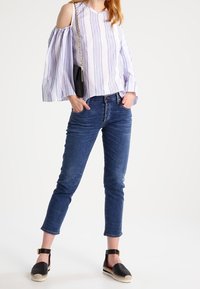 Randig, off-shoulder blus i vitt och blått; kombinerad med slim-fit blå jeans och svarta espadrill-wedges med ankelremmar.