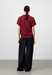 Top corto bordeaux a maniche corte con scollo rotondo, abbinato a pantaloni larghi blu navy a gamba larga, che mostrano texture morbide e silhouette rilassate.
