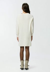 Abito bianco a maniche lunghe e coste con vestibilità rilassata, che arriva a metà coscia, abbinato a stivaletti grigi alla caviglia e collant neri trasparenti.