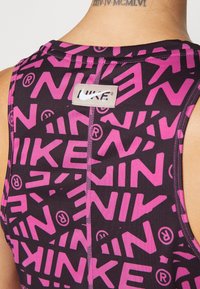 Černý sportovní tank top s opakujícím se vzorem růžového loga Nike, kulatým výstřihem a plochými švy. Visačka viditelná na zadní straně.