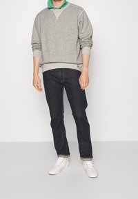 Gray sweatshirt with a green collar layered underneath, paired with dark blue jeans and white sneakers. Simple design and relaxed fit.