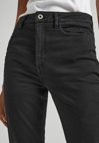 Jeans in denim nero caratterizzati da un design aderente, tasche standard e chiusura con bottone metallico, con dettagli di cucitura visibili.