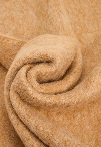 Un tissu doux de couleur camel, avec une texture pelucheuse, enroulé en couches, mettant en valeur son matériau épais et chaleureux, idéal pour des couvertures ou des vêtements.