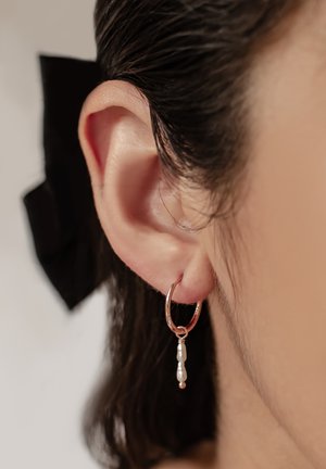 Rose gold hoop earring with a delicate chain, featuring a small white pearl and a round metallic accent. Close-up on ear.