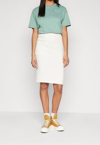 Tyrkysové bavlněné tričko, bílé sukňové šaty ke kolenům a žluté tenisky s vysokým střihem a bílou podrážkou; s přední kapsou.