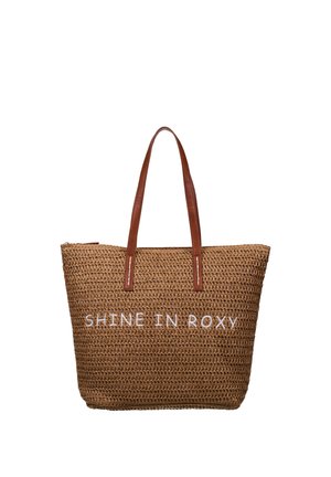 Sac fourre-tout tissé marron avec deux anses en cuir marron et texte blanc brodé "SHINE IN ROXY" à l'avant.