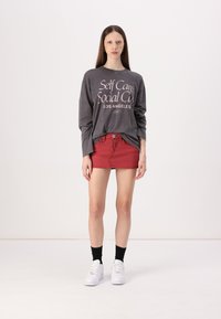 Grå langermet skjorte med hvit tekst, kombinert med et rødt denim miniskjørt. Modellen har på seg hvite sneakers og svarte sokker. Enkelt design.