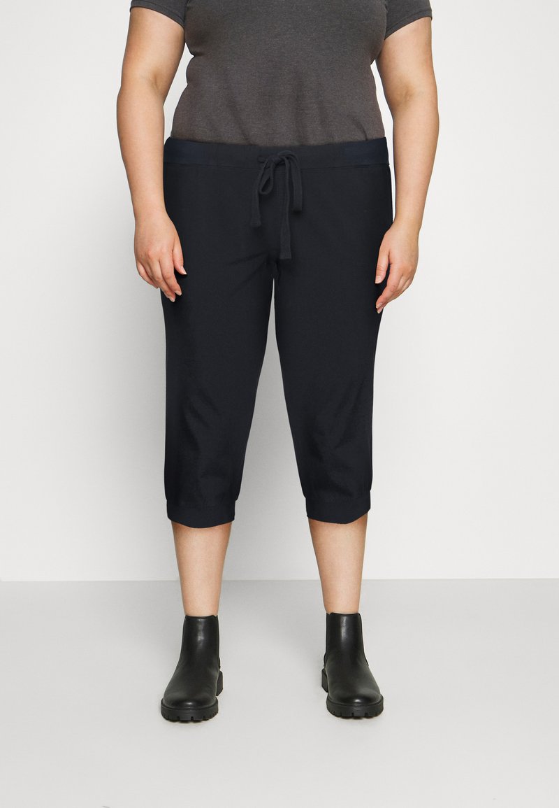 Zwarte capri-broek met een trekkoord in de taille, een gladde textuur en een cropped lengte, gecombineerd met zwarte enkellaarsjes.