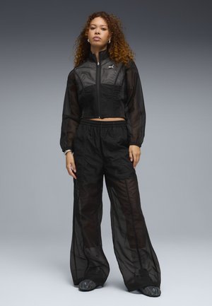 Sort gennemsigtigt træningssæt med en croppet lynlåstrøje og løstsiddende bukser. Har tekstureret stof og et lille logo på brystet.